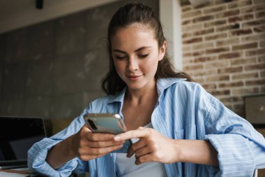 Oturma odasında otururken akıllı telefon kullanan konsantre bir kızın fotoğrafı.