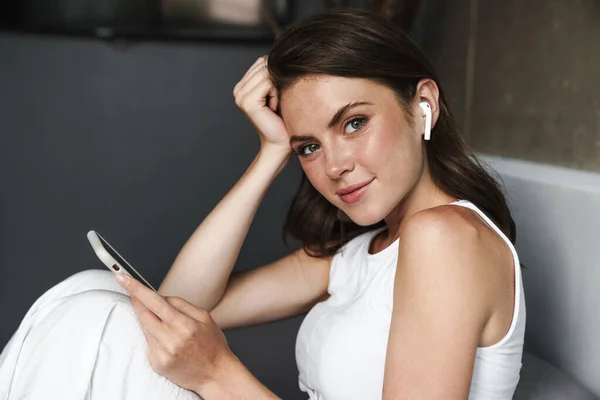 Imagen Mujer Atractiva Morena Usando Auriculares Inalámbricos Teléfonos Inteligentes Mientras —  Fotos de Stock