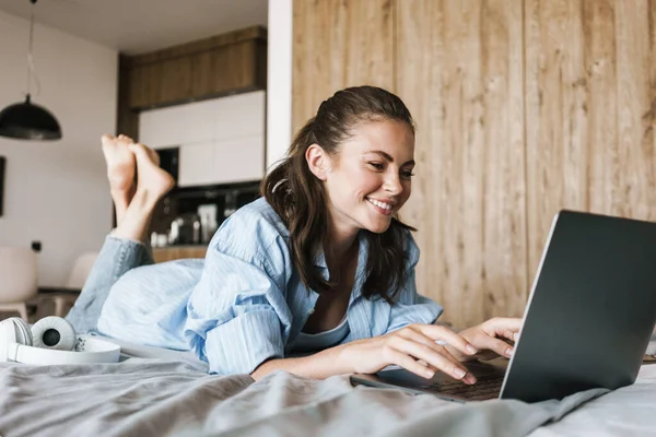 집에서 노트북 컴퓨터를 사용하여 침대에 행복하게 소녀의 — 스톡 사진