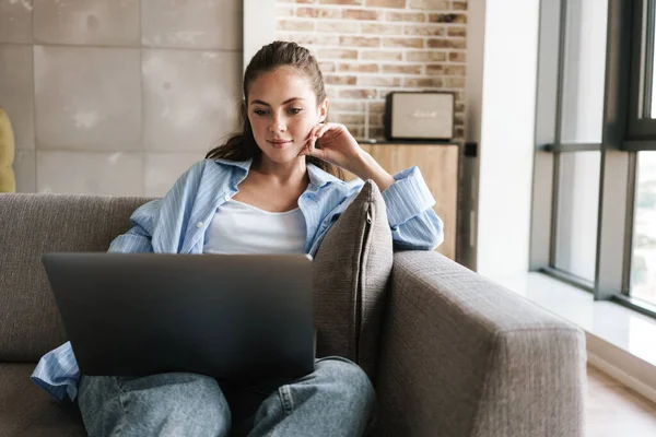 Foto Menina Agradável Satisfeito Usando Laptop Enquanto Sentado Sofá Sala — Fotografia de Stock