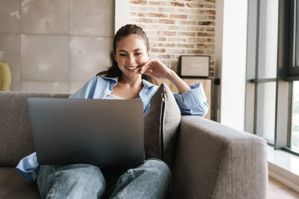 Foto Alegre Chica Agradable Sonriendo Usando Ordenador Portátil Mientras Está —  Fotos de Stock