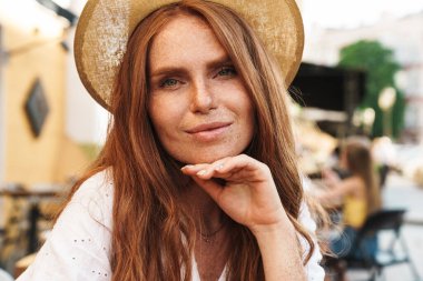 Güzel, gülümseyen, kızıl saçlı kadının yakın çekimde kafede oturup kameraya bakmasını.