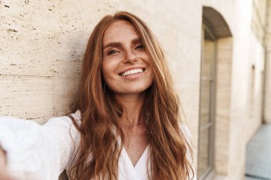 Şehirde yürürken gülümseyen ve selfie çeken neşeli kızıl kadın görüntüsü