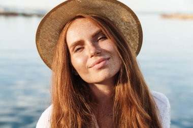 Şapkalı, neşeli kızıl bir kadının görüntüsü. Gülümseyen ve gezinti güvertesinde yürürken kameraya bakan.