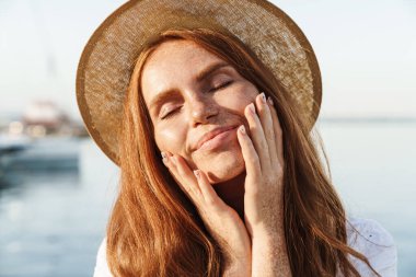 Gezintide yürürken gözleri kapalı gülümseyen şapkalı neşeli kızıl kadın görüntüsü