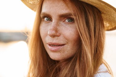 Şapkalı, poz veren ve gezinti güvertesinde yürürken kameraya bakan kızıl bir kadın resmi