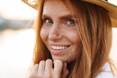 Şapkalı neşeli kızıl saçlı bir kadının görüntüsü gülümseyen ve gezinti güvertesinde kameraya bakan.