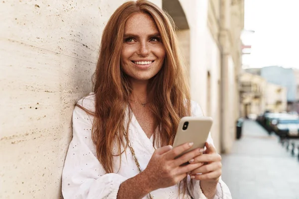 Imagen Alegre Pelirroja Sonriendo Usando Teléfono Móvil Mientras Camina Por — Foto de Stock