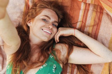 Yazlık elbiseli, battaniyeye uzanmış, selfie çeken genç bir kızın en iyi görüntüsü.