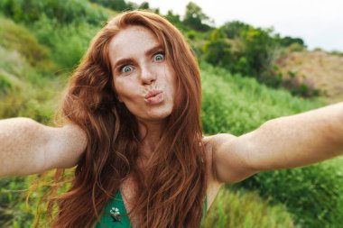 Genç, mutlu, güzel bir kadın yeşil dosyada dururken selfie çekiyor.