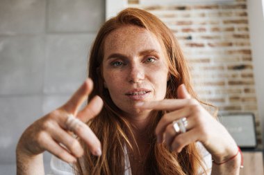 Ciddi kızıl saçlı, çilli bir kadının evdeki kamerayı işaret edişi.