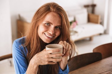 Çekici, gülümseyen bir kadın kafede otururken bir fincan kahve içiyor.