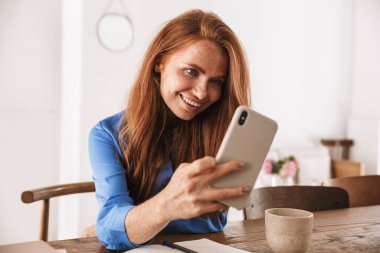 Kafede dinlenirken ve bir fincan kahve içerken akıllı telefonuyla selfie çeken güzel, genç bir kadın.