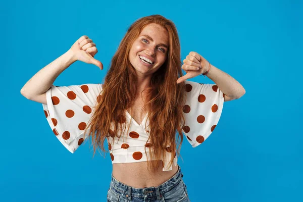 Yazlık giysiler içindeki güzel genç bir kadın, parmaklarıyla kendini işaret ediyor, mavi arka plan için tek başına duruyor.