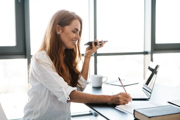 Wizerunek Szczęśliwej Bizneswoman Pracującej Telefonu Komórkowego Laptopa Podczas Zapisywania Notatek — Zdjęcie stockowe