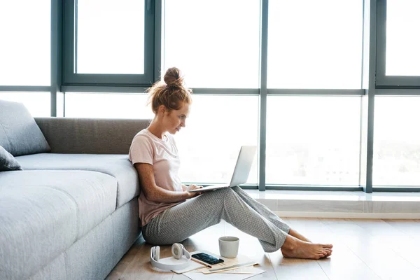 Afbeelding Van Gerichte Roodharige Vrouw Werken Met Laptop Terwijl Zitten — Stockfoto