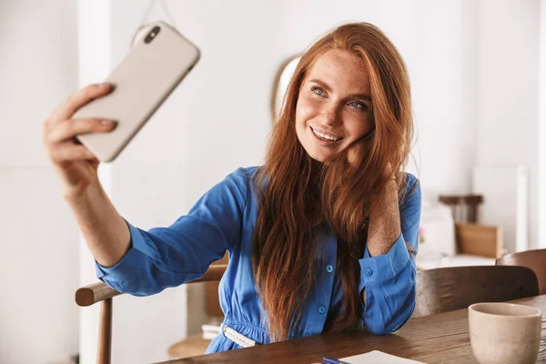 Kafede dinlenirken ve bir fincan kahve içerken akıllı telefonuyla selfie çeken güzel, genç bir kadın.