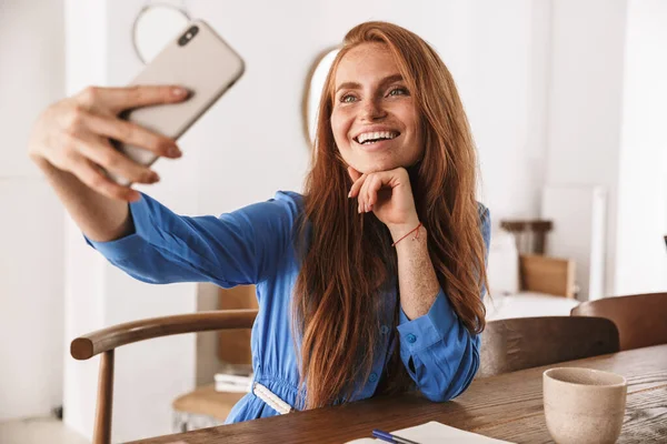 Kafede dinlenirken ve bir fincan kahve içerken akıllı telefonuyla selfie çeken güzel, genç bir kadın.