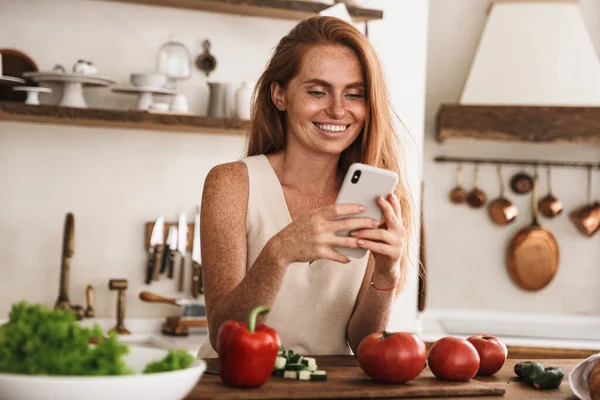 Sorrindo Atraente Jovem Mulher Usando Telefone Celular Enquanto Estava Cozinha — Fotografia de Stock