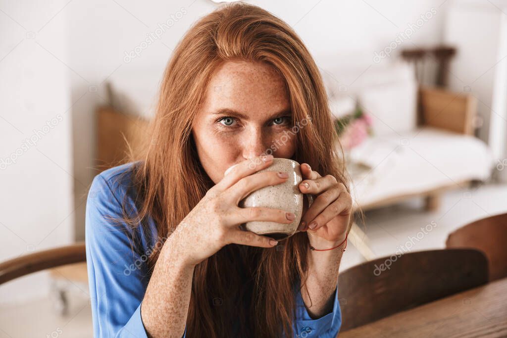 Attractive young smiling woman having cup of coffee while sitting in the cafee indoors