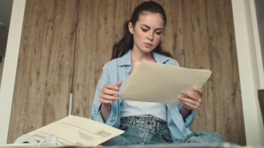 Ciddi bir kadın evde otururken kağıt belgelerle çalışıyor.