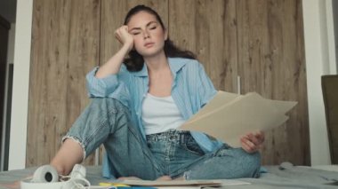 Sıkılmış bir kadın evde otururken kağıt belgelerle çalışıyor.