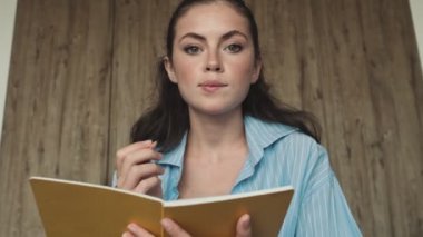 Güzel bir genç kadın, evinde yatak odasında kameraya bakarken notlar alıyor.