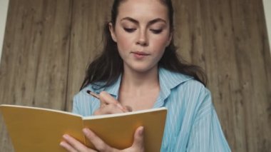 Çekici genç bir kadın, fotokopi kitabına yazarken yatak odasında kameraya bakıyor.