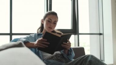 Sakin genç bir kadın evde oturmuş kitabını okuyor.