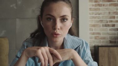 Kulaklık takan genç ve güzel bir kadın internette dizüstü bilgisayarını kullanarak evdeki masada oturuyor.