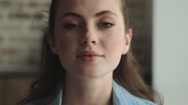 Pozitif genç bir kadının yakın çekim görüntüsü evde otururken gülümsemesidir.