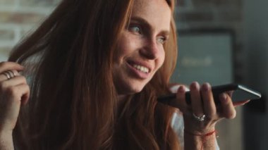 Evde cep telefonuyla konuşan mutlu, genç bir kızıl kadın.