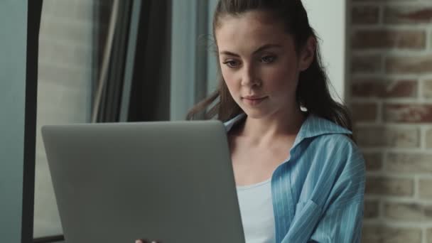 美しい若い女性は自宅に立っている間 彼女のラップトップコンピュータを使用しています — ストック動画