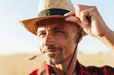 Ağzında buğday kulağı olan ve mısır gevreği tarlasında dikilen gülümseyen yetişkin bir adamın görüntüsü.