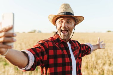 Hasır şapkalı heyecanlı bir yetişkinin mısır gevreği tarlasında cep telefonuyla selfie çekmesi.
