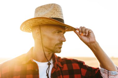 Hasır şapkalı, mısır gevreği tarlasında dikilirken yana bakan erkeksi bir adam.