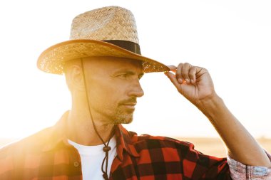 Hasır şapkalı, mısır gevreği tarlasında dikilirken yana bakan erkeksi bir adam.