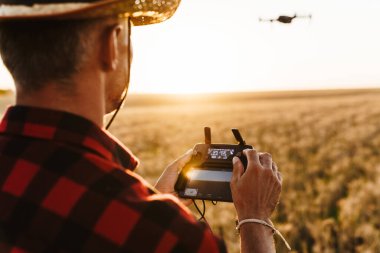 Hasır şapkalı odaklanmış bir adamın mısır gevreği tarlasında dikilirken dron kullanmasının görüntüsü