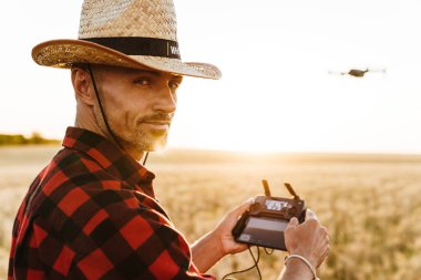 Hasır şapkalı yakışıklı bir adamın mısır gevreği tarlasında dron kullanırken görüntüsü