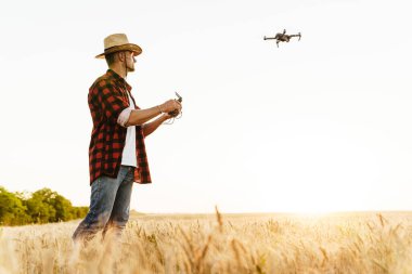 Hasır şapkalı yakışıklı bir adamın mısır gevreği tarlasında dron kullanırken görüntüsü