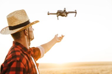 Hasır şapkalı yakışıklı bir adamın mısır gevreği tarlasında dron kullanırken görüntüsü
