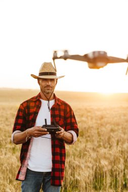 Hasır şapkalı yakışıklı bir adamın mısır gevreği tarlasında dron kullanırken görüntüsü