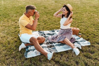 Yaz parkında çimlerin üzerinde otururken eski bir kamerada güzel bir kadının fotoğrafını çeken orta yaşlı yakışıklı bir adam.
