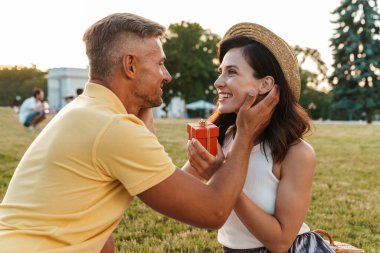 Yakışıklı, olgun, kır saçlı bir adamın görüntüsü dışarıda, güzel yeşil bir doğa parkında kadınına hediye veriyor..