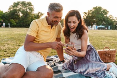 Güzel yeşil bir doğa parkında cep telefonu kullanan, şok olmuş, iyimser, sevgi dolu bir çiftin görüntüsü..