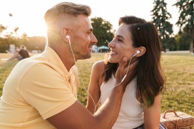 Orta yaşlı mutlu bir çiftin portresi. Yaz parkında oturmuş kulaklıkla gülümseyen ve müzik dinleyen bir çift.