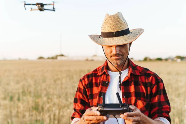 Hasır şapkalı yakışıklı bir adamın mısır gevreği tarlasında dikilirken dron kullanması.