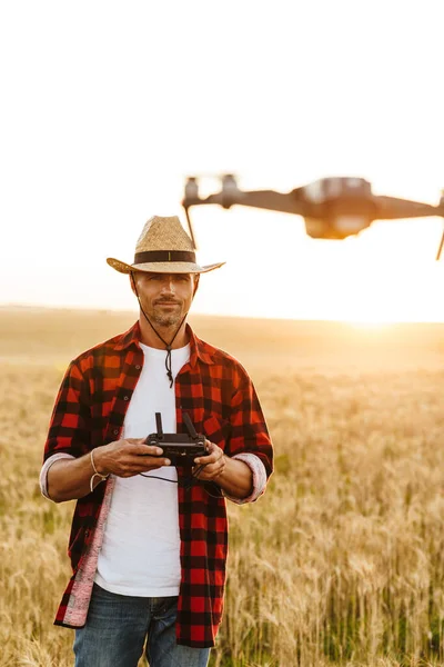 Hasır şapkalı yakışıklı bir adamın mısır gevreği tarlasında dron kullanırken görüntüsü