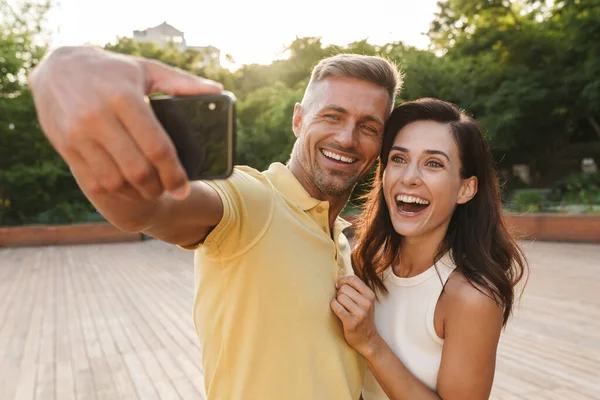 一对兴奋的成年男女在夏季公园散步时 用手机拍照和大笑的肖像 — 图库照片