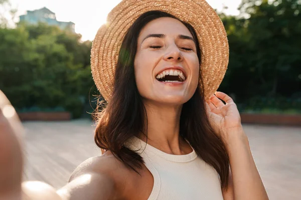 夏の公園を歩きながら自撮り写真を撮り笑いながら藁帽子をかぶった素敵な中年女性のイメージ — ストック写真